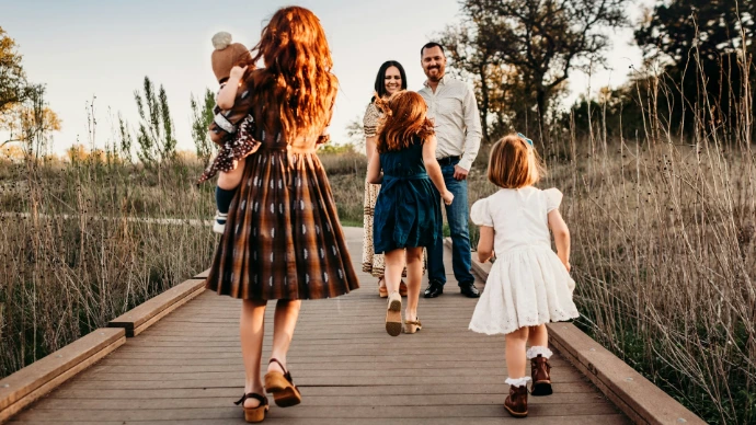 A family walking along a wooden boardwalk in a field during golden hour
